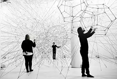 Adults in a bright white room, interacting with wires going from floor to ceiling