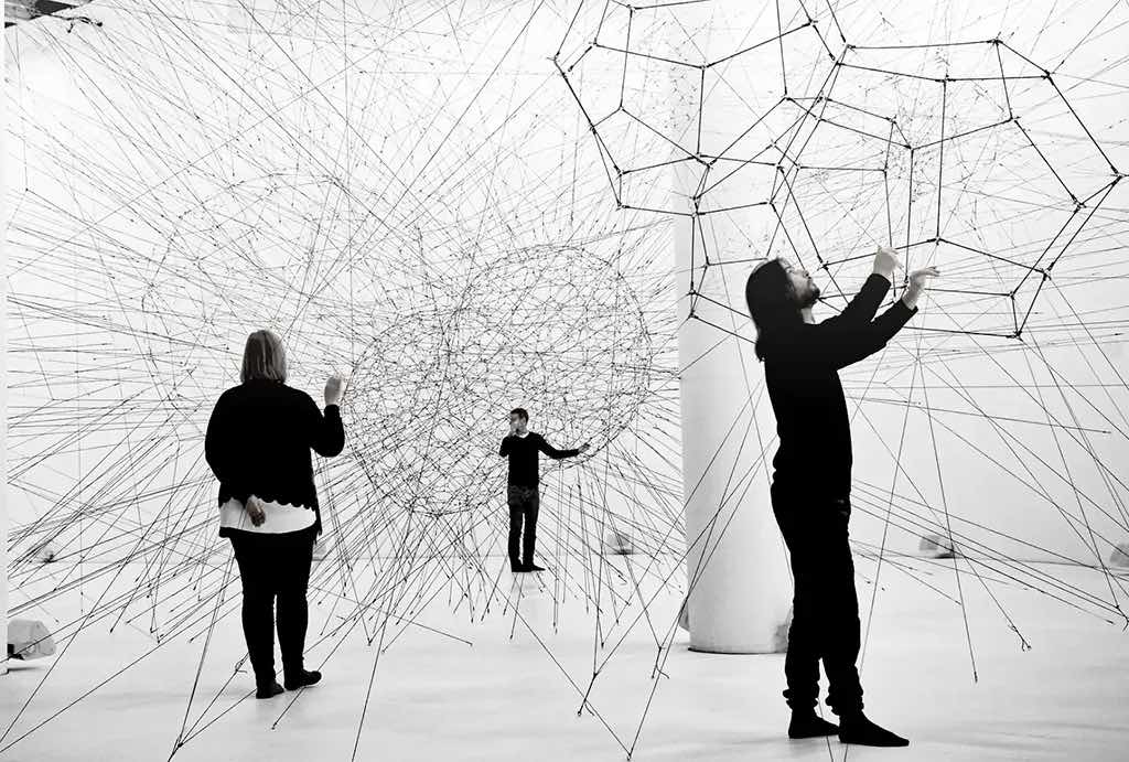 Three adults looking at an installation of diagonal lines going through in a big white space